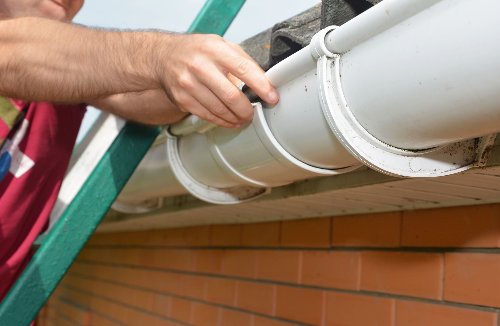 Roof gutter installation. A man on a ladder is installing a roof gutter"u2019s slip joint connector to connect the gutters and avoid water leaks.